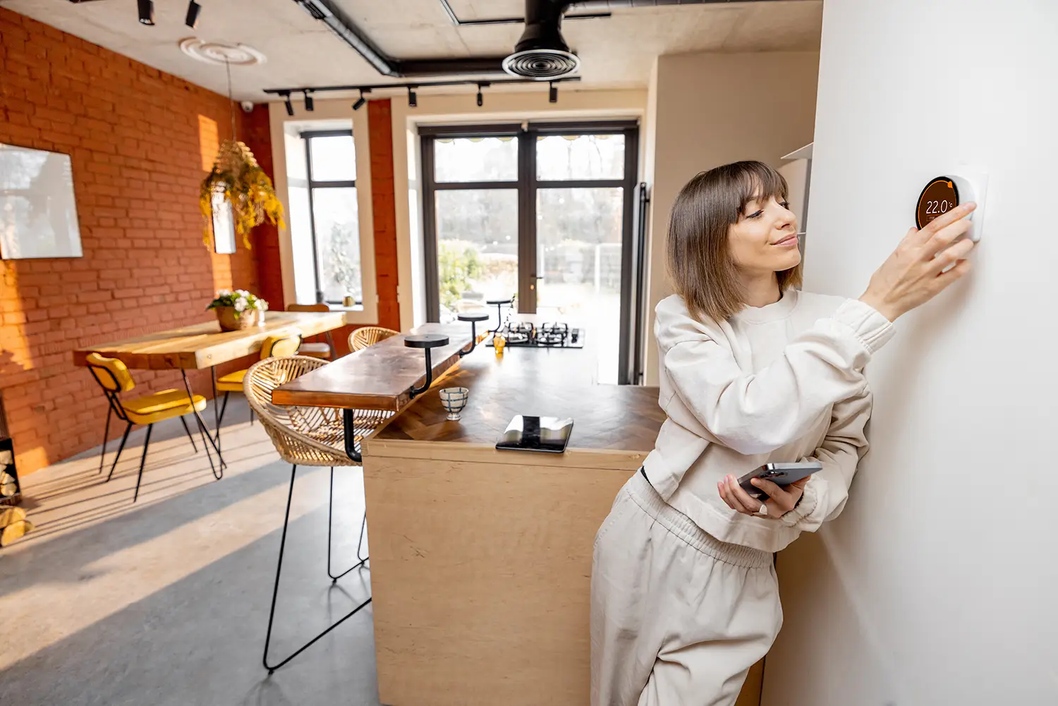 Eine Frau regelt die Temperatur in ihrem Haus mit einem elektronischen Thermostat, der im Wohnzimmer an der Wand montiert ist.